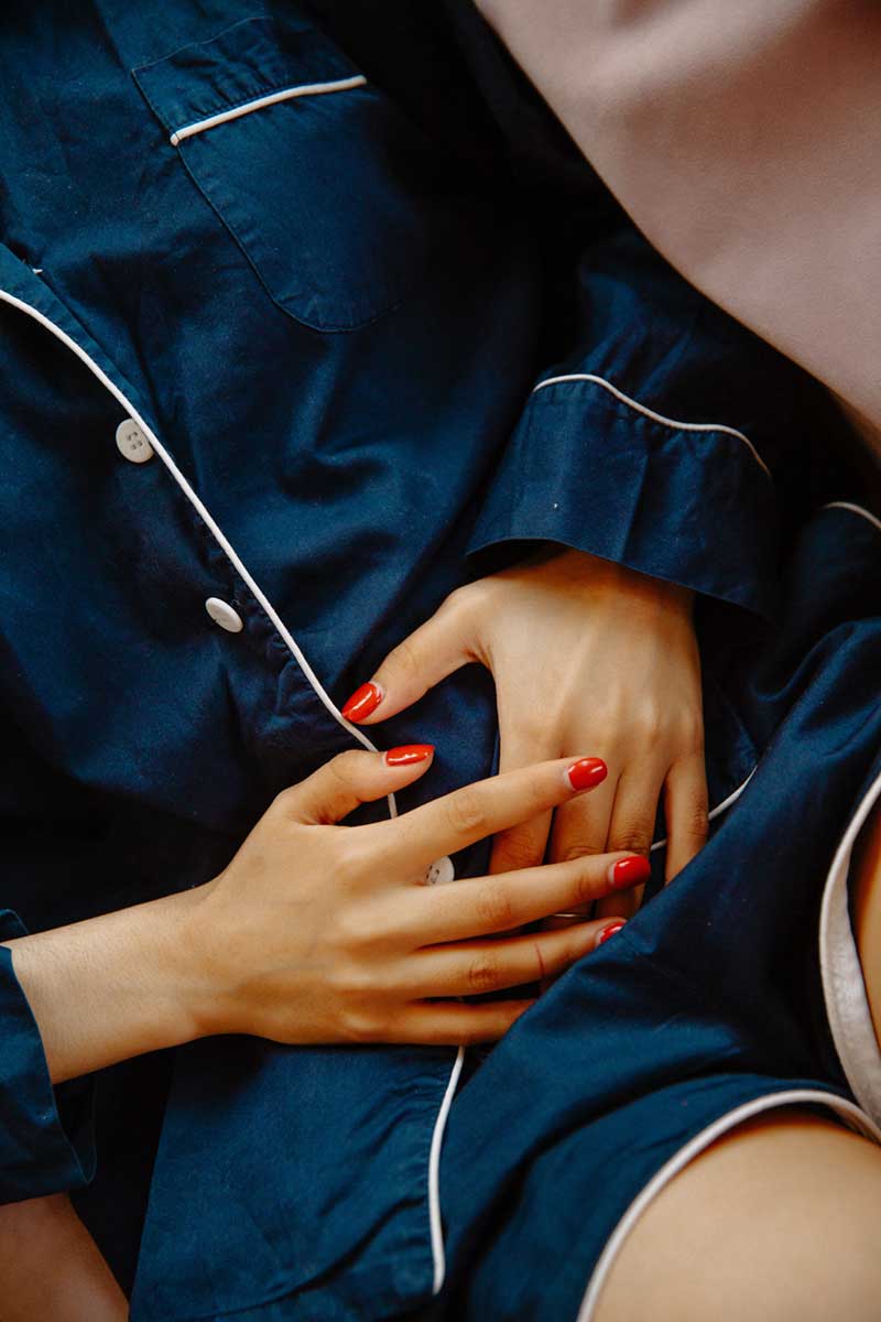 a woman's body in blue pajamas with hands over abdomen indicating cramps
